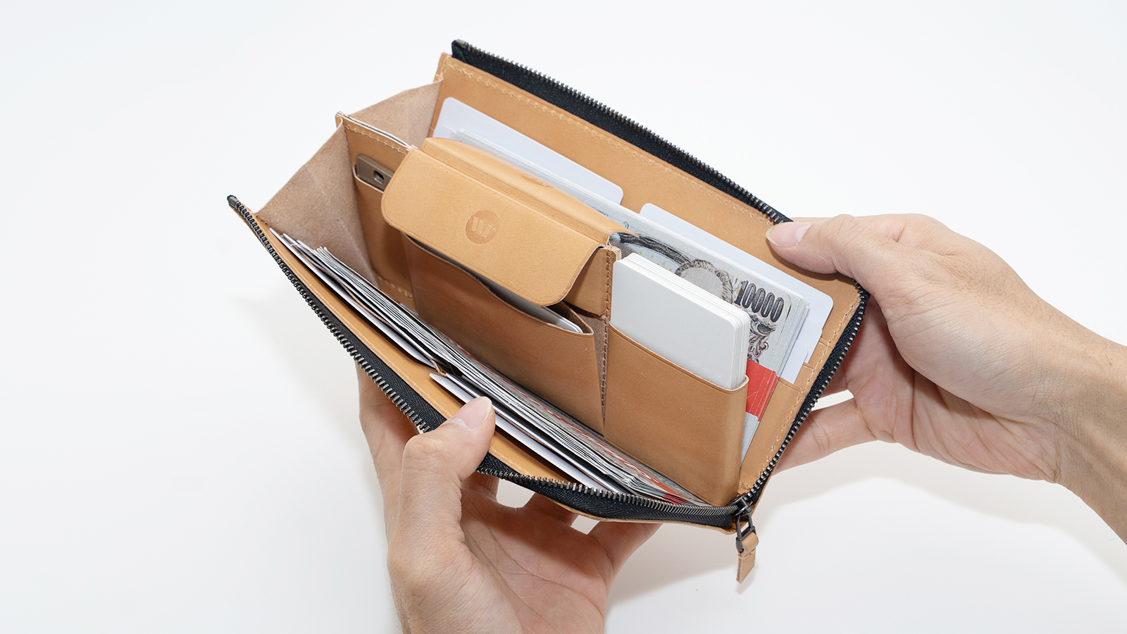 Open tan leather wallet showing card slots and folded cash, held by hands against a white background, zipper closed behind.
