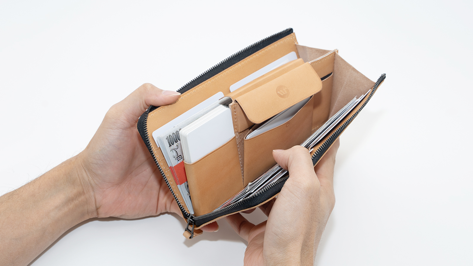 Open brown leather zippered wallet held by hands, exposing credit cards and folded cash inside.