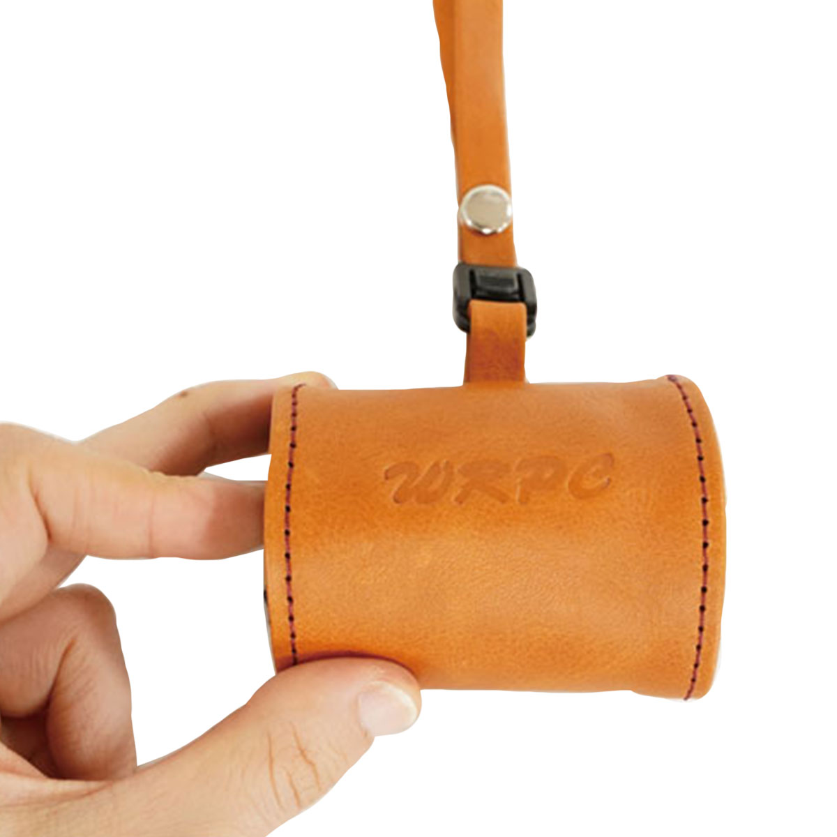 Hand holding a small tan leather cylindrical pouch with a strap and stitched edges, embossed lettering on the side.