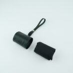 Dark leather cylindrical bag with a short strap and metal button on a pale surface
