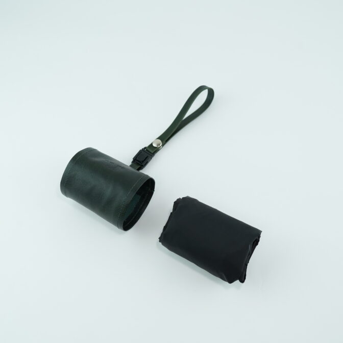 Dark leather cylindrical bag with a short strap and metal button on a pale surface