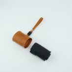 Tan leather strap with a metal rivet attached to a small cylindrical leather pouch, lying on a light surface with a black fabric pouch nearby.