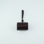 Small brown leather wallet or pouch with a wrist strap against a pale background.