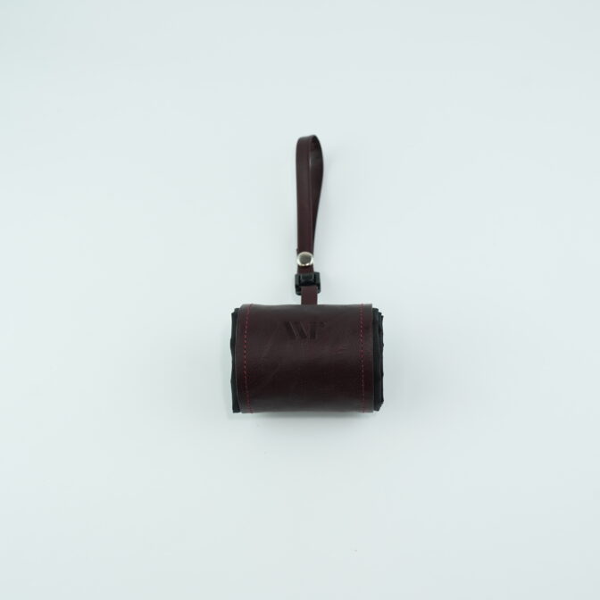 Small brown leather wallet or pouch with a wrist strap against a pale background.