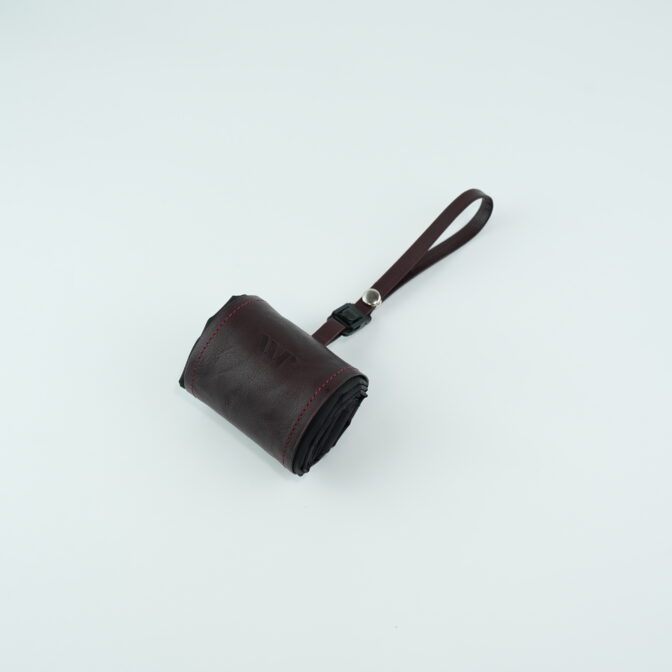 Small burgundy leather pouch with a matching wrist strap on a pale surface, likely a compact wallet or case.