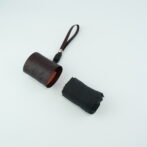 Brown leather cylindrical pouch with red stitching and a looped brown strap on a light background