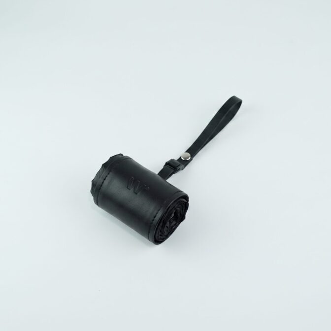 Rolled black leather pouch with a strap on a light background, partially visible in the frame.